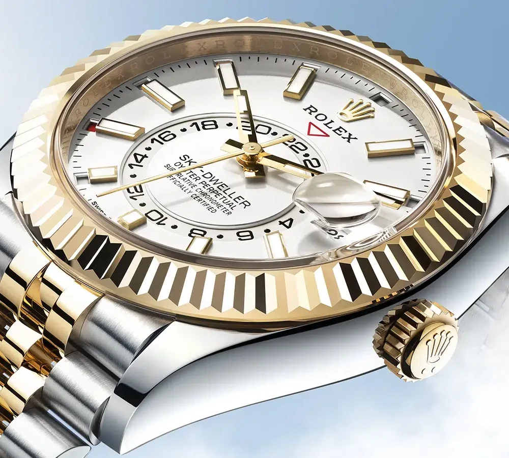 Close-up of a Rolex Sky-Dweller watch with a fluted bezel, white dial, and two-tone bracelet against a sky blue background.