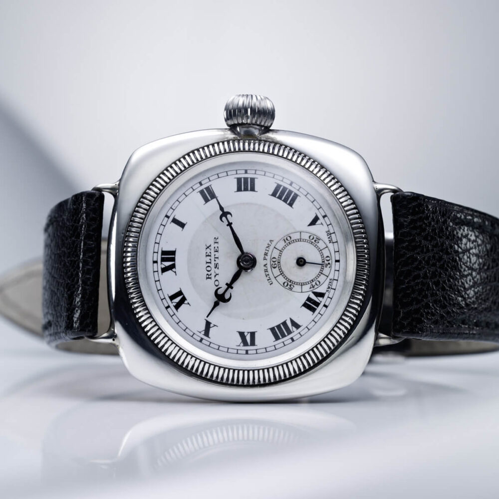 An elegant wristwatch with a rectangular white dial, Roman numerals, and a black leather strap, placed against a soft gray background.