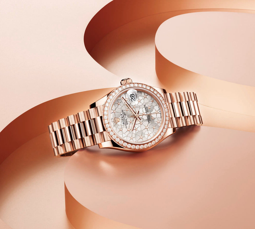 Luxury rose gold wristwatch with a detailed, jeweled face displayed on a curved, abstract pink background.