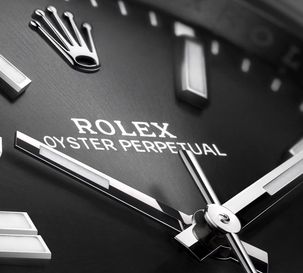 Close-up of a Rolex Oyster Perpetual watch face, highlighting the brand logo and silver-tone hands and hour markers.