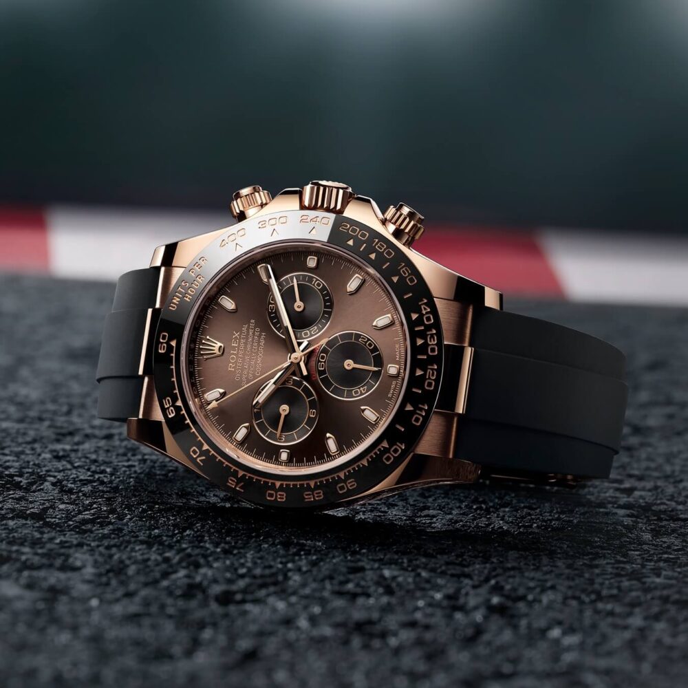 A luxurious rose gold chronograph watch with a black rubber strap, placed on a textured surface, emphasizing its elegant design and sophisticated detailing.