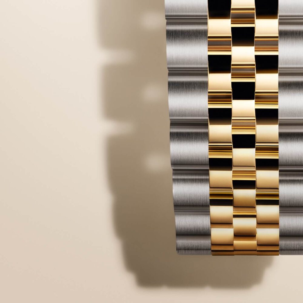 A series of metallic ribbons including silver and gold, neatly arranged in parallel lines with a soft shadow on a light beige background.
