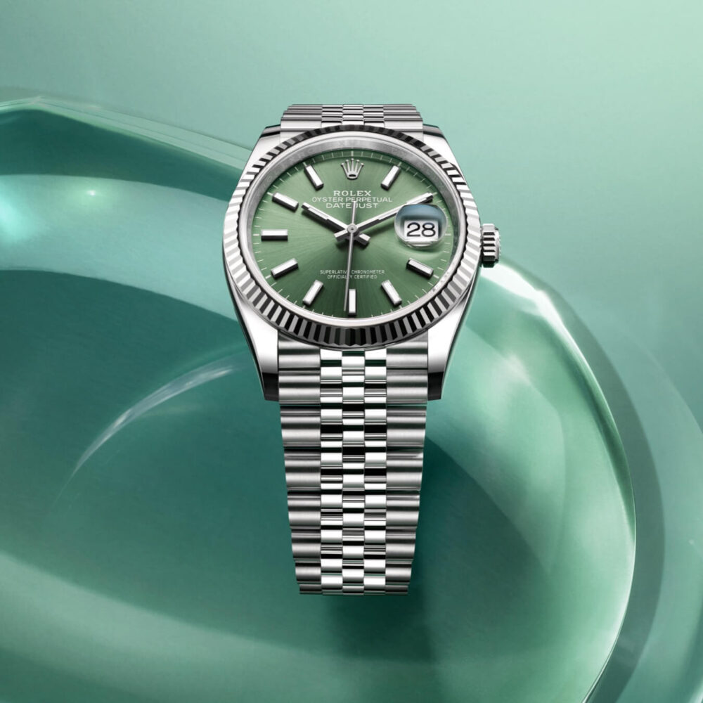 A Rolex Datejust watch with a green face and a stainless steel Jubilee bracelet, set against a light green background.