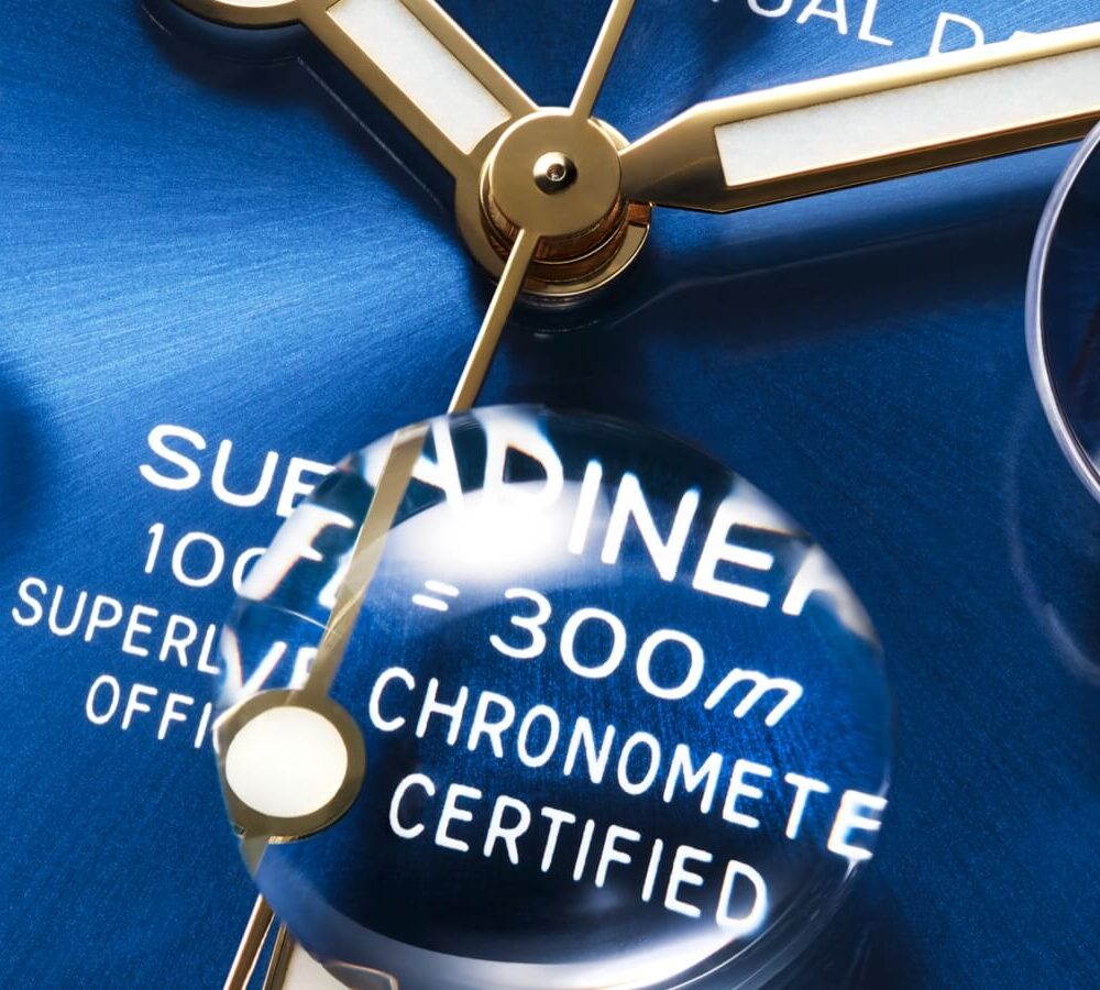 Close-up of a luxury watch dial under a magnifying glass, highlighting the text "Superlative Chronometer Certified" and water resistance details.