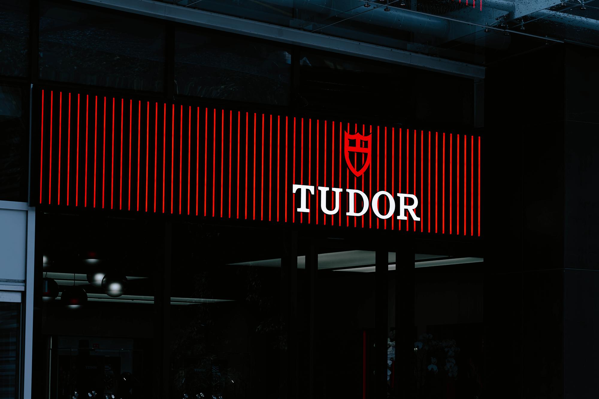 Illuminated red and white "TUDOR" sign with logo on a building facade at night.
