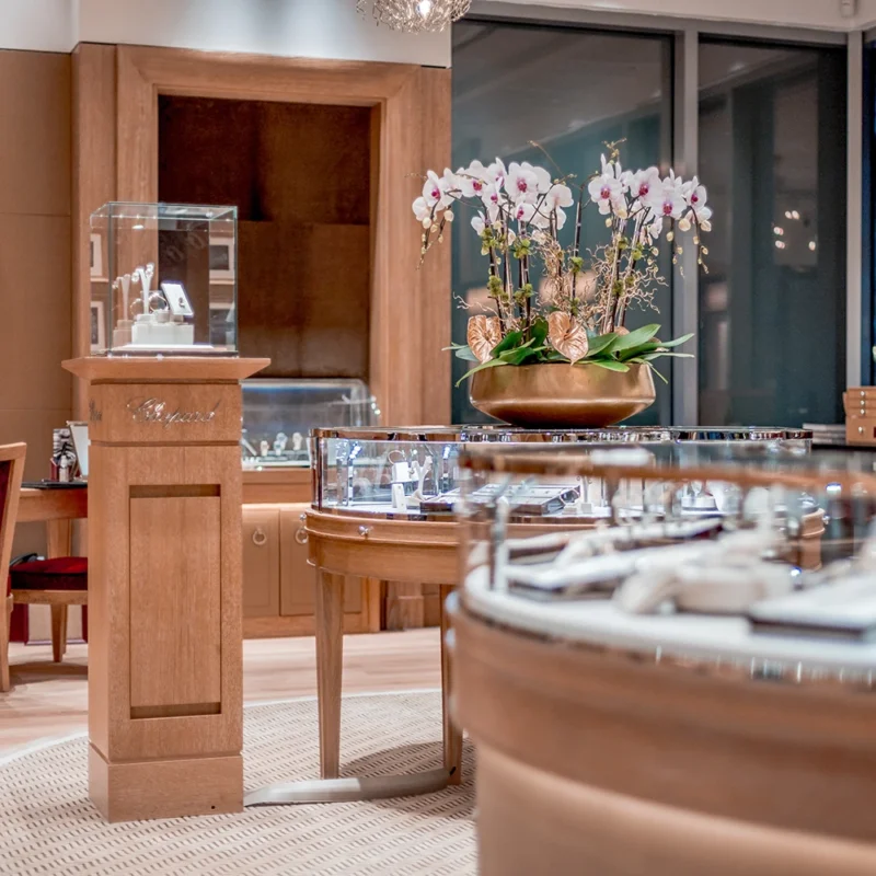Elegant jewelry store interior with wooden display cases, orchids in a bowl on a pedestal, and a chandelier.