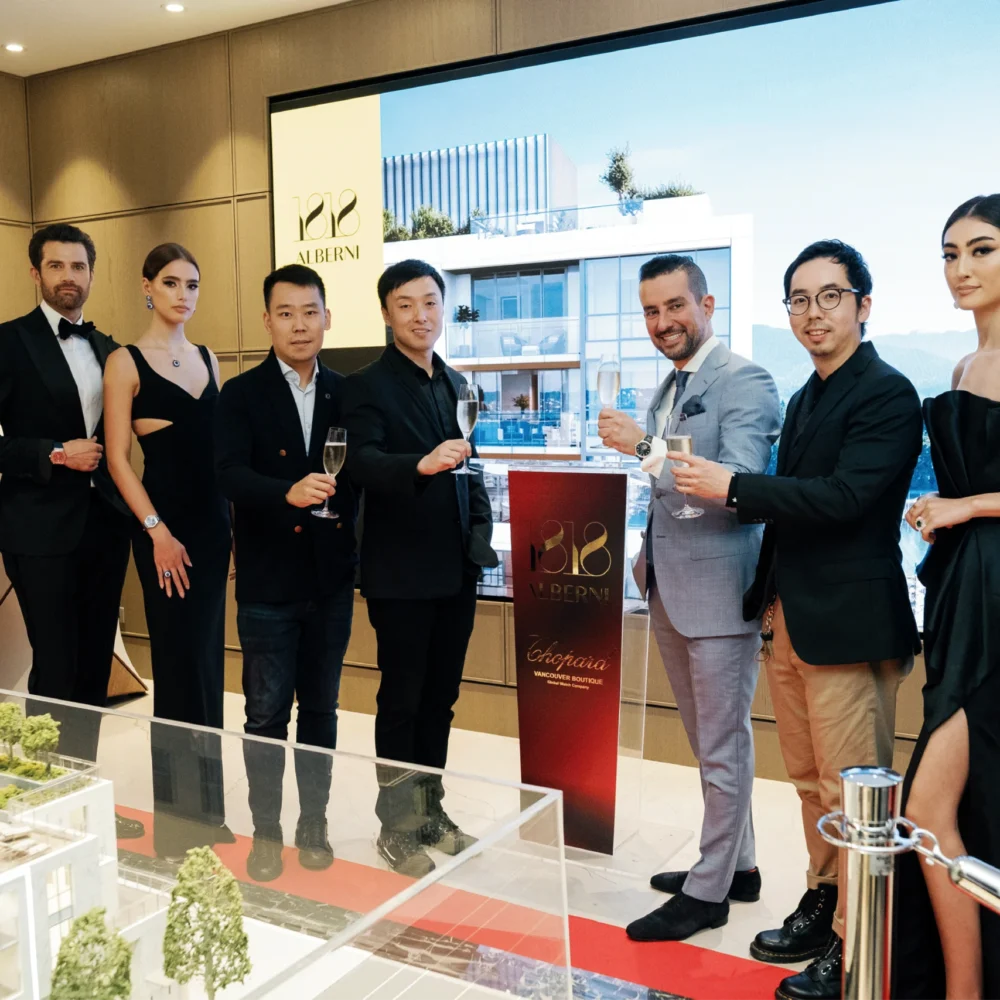 Group of seven people, dressed in formal attire, standing around a model building display at a real estate event.