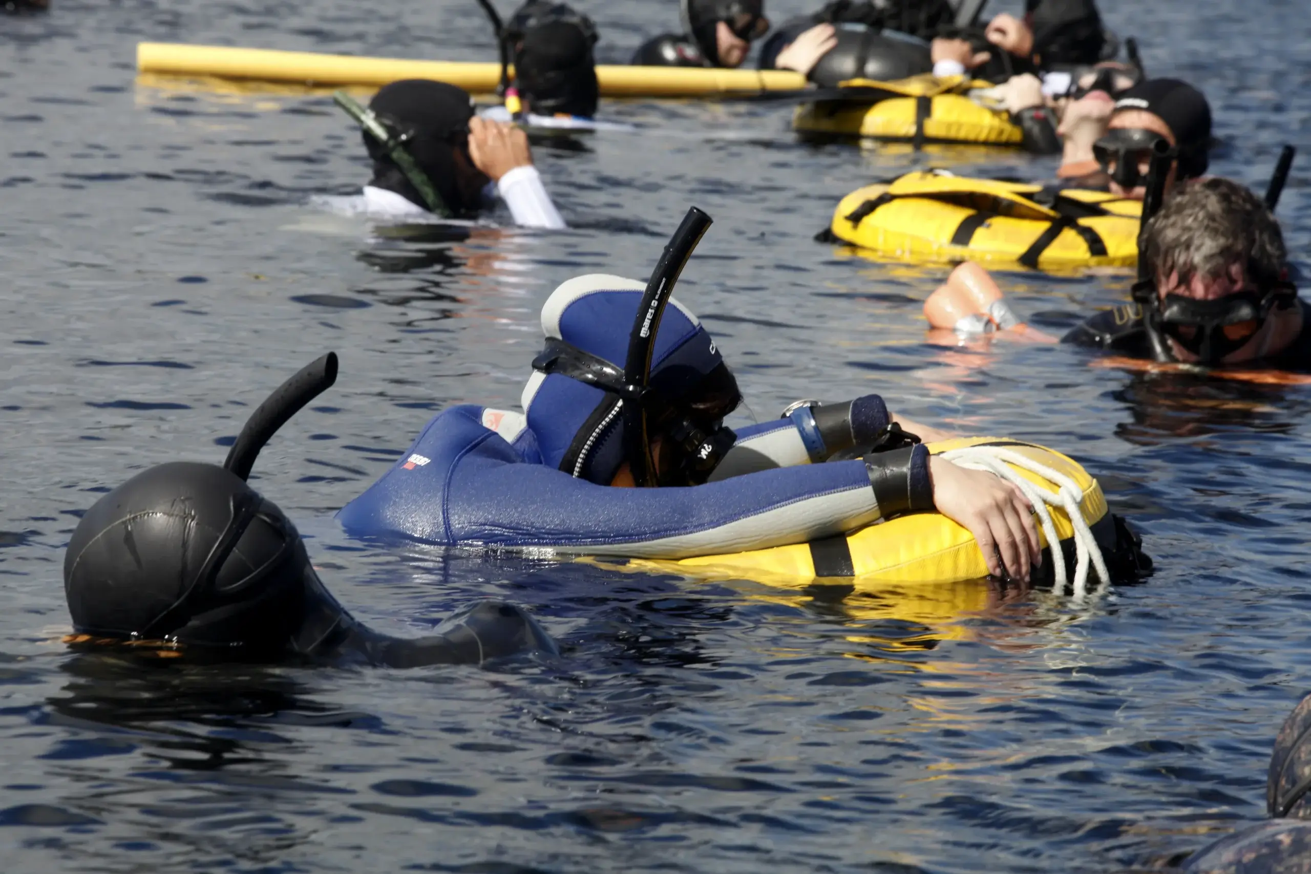 Scuba divers in wet suits and snorkeling gear floating on the surface of water during a training session.