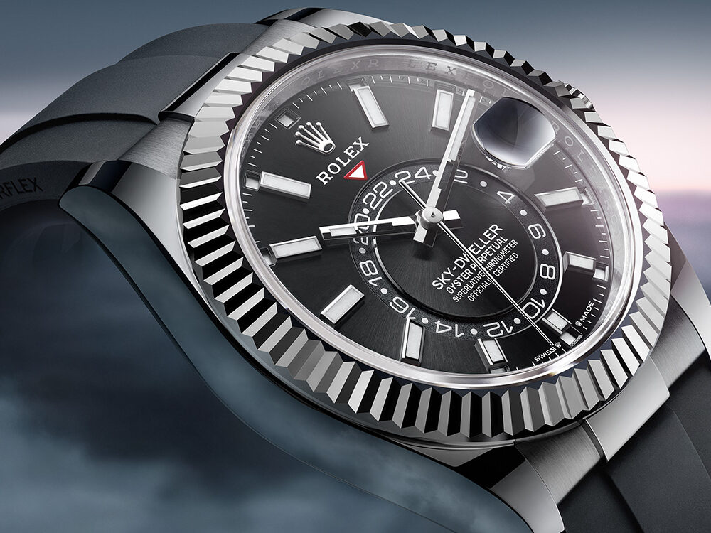 Luxury wristwatch with a black dial and silver bezel presented against a misty seascape at dusk.