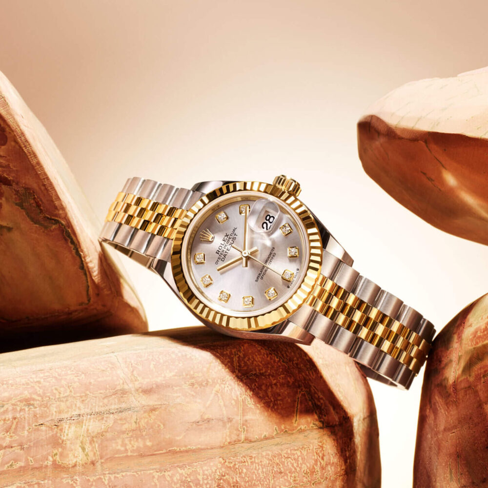 A luxury watch with a gold and silver band, displayed on polished, sculpted stone under soft lighting.