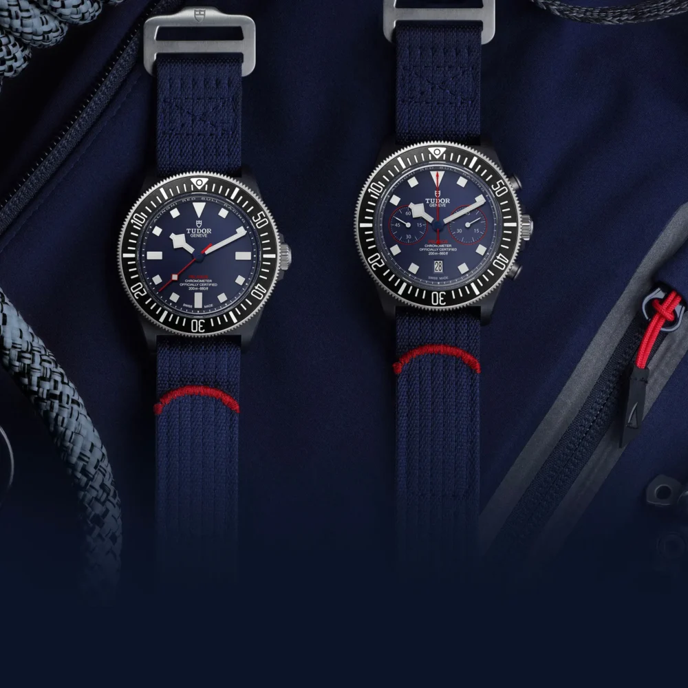 Two wristwatches with navy blue straps next to a backpack and earphones on a dark fabric background.