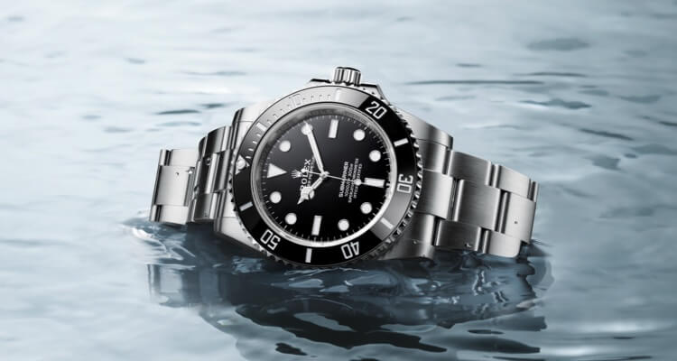 Stainless steel diver's watch with a black bezel and dial, partially submerged in water, reflecting light on its surface.