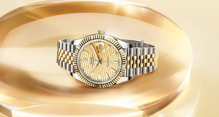 Luxury wristwatch with a gold and silver band, featuring a gold dial with intricate detailing, displayed against a soft golden background.