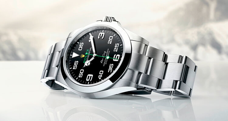 Stainless steel wristwatch with a black dial featuring green and white accents, set against a blurred snowy mountain background.