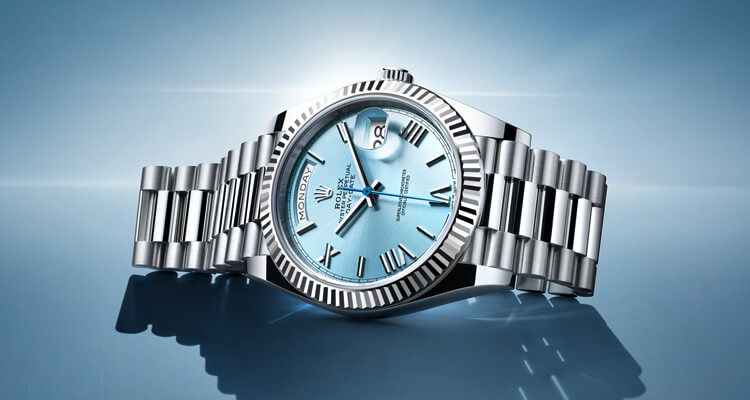 A luxury watch with a turquoise face and stainless steel bracelet against a blue gradient background.