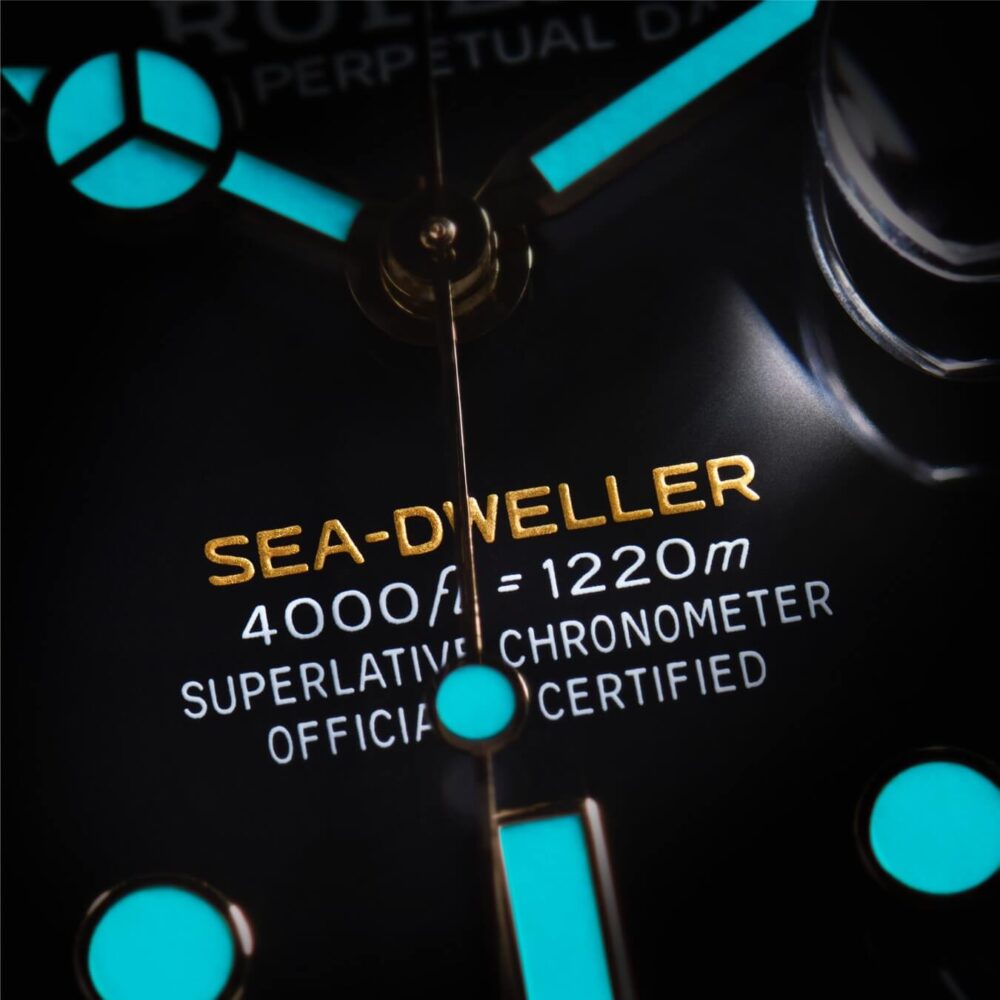 Close-up of a Rolex Sea-Dweller watch face showing luminous hour markers and text detailing its 4000ft/1220m water resistance.