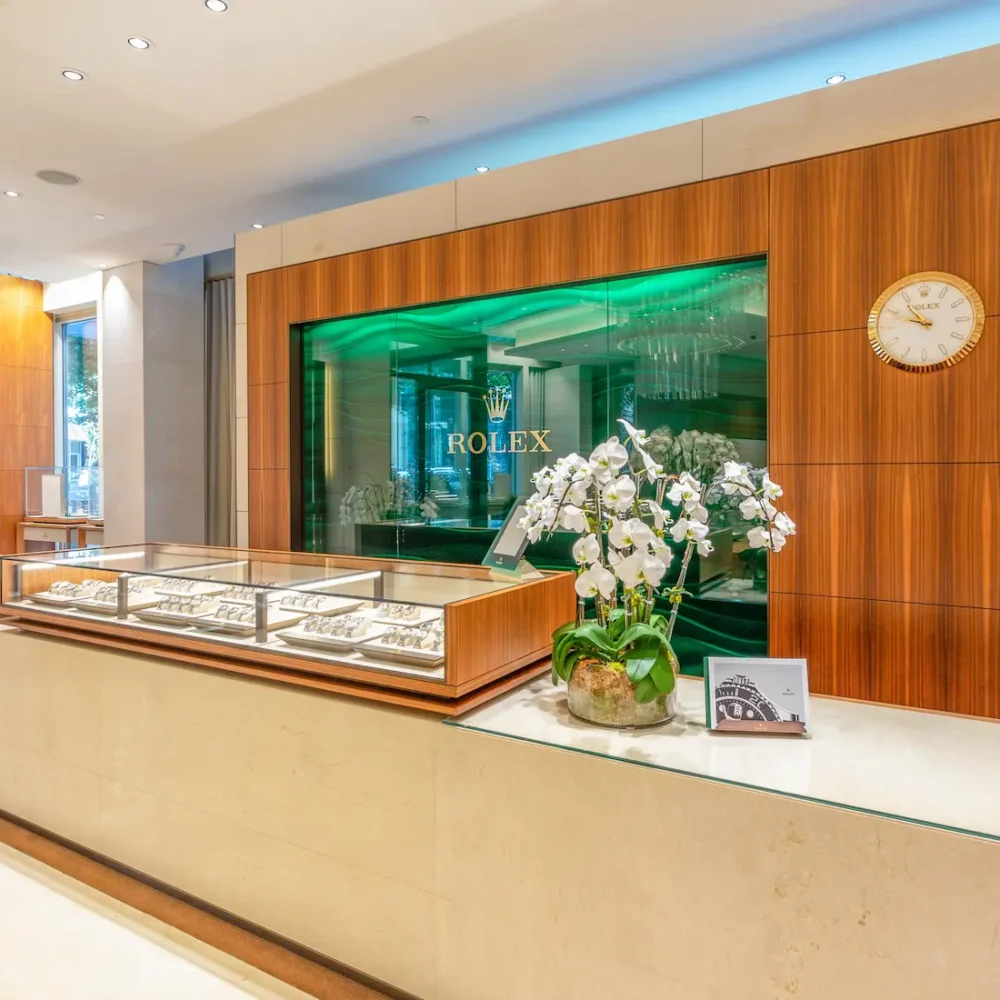 Interior of a Rolex store with elegant wooden walls, display cases of watches, white flower arrangement, and a wall clock.