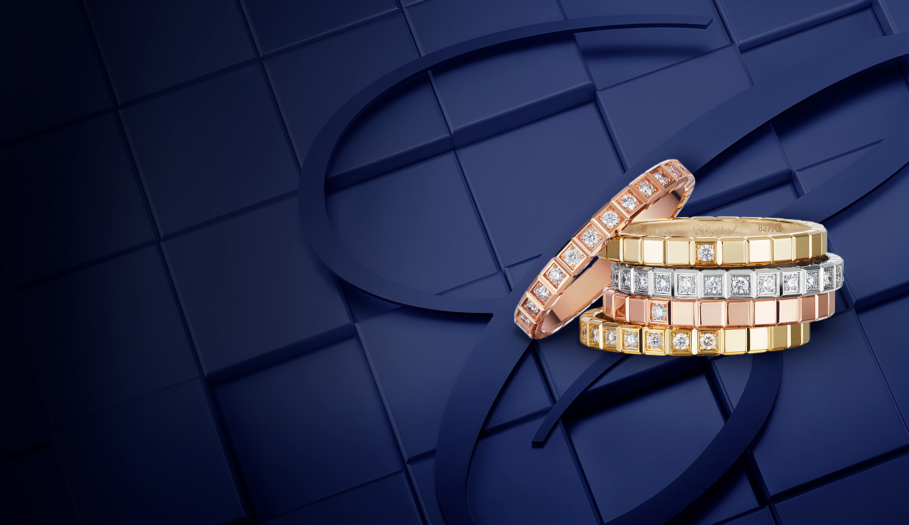Stacked luxury rings with diamonds on a blue geometric background. The rings are in rose, yellow, and white gold, featuring square and rectangular gem settings.