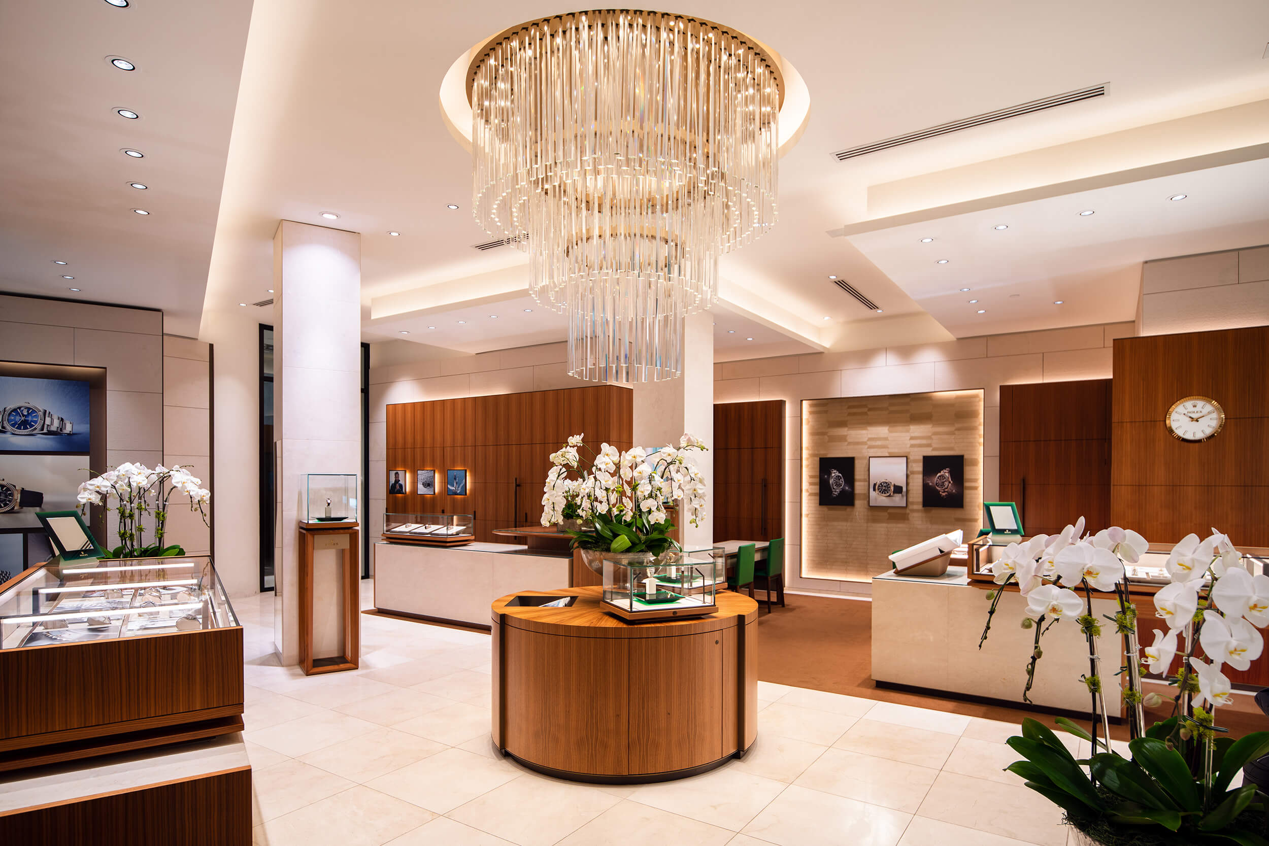 Elegant jewelry store interior with wooden display counters, a striking chandelier, and orchids, under warm lighting.