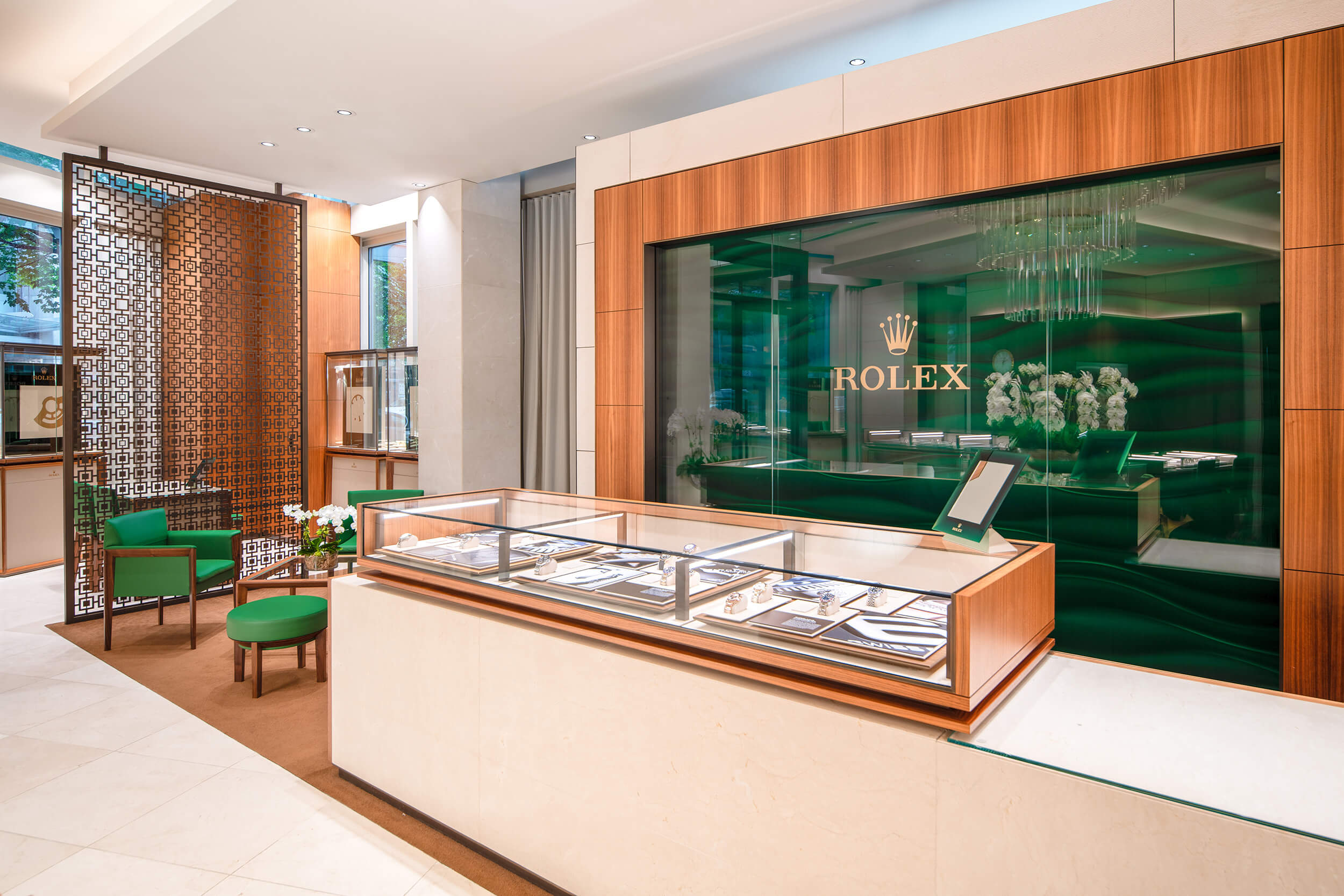 Interior of a Rolex store with elegant display cases, green decor, and a prominent Rolex logo on the back wall.